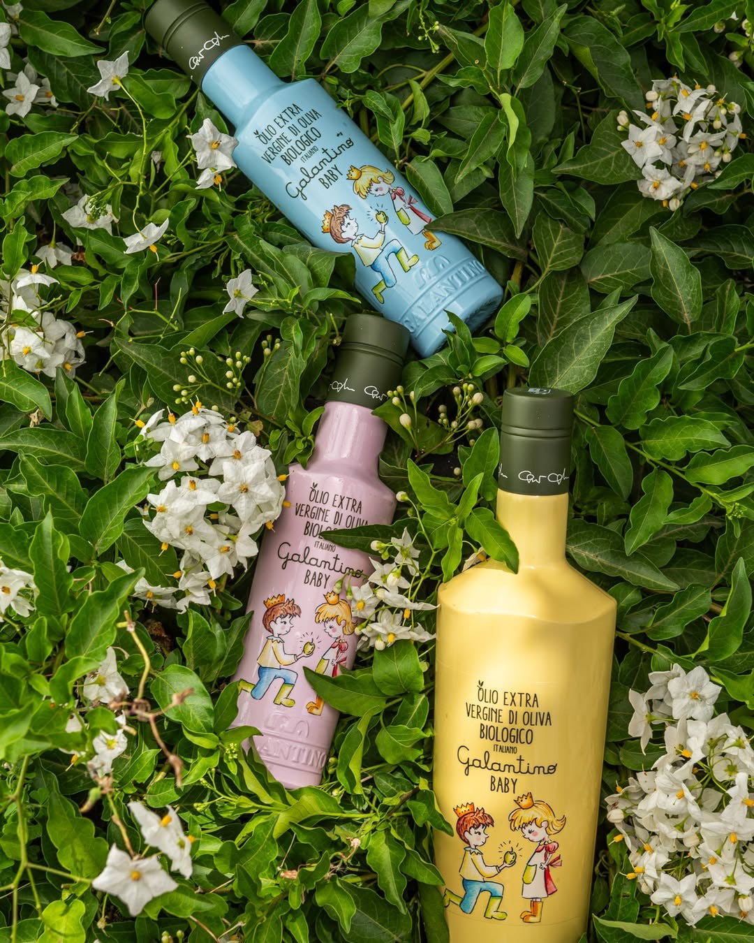 Drie kleurrijke flessen Galantino olijfolie – blauw, roze en geel – sfeervol gepresenteerd in het gras, ideaal voor baby’s en kinderen.